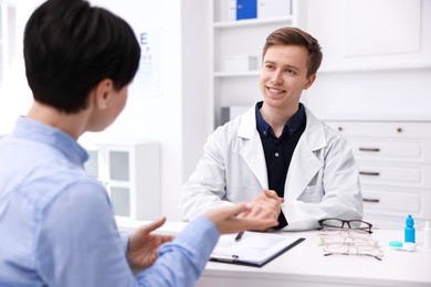 Photo of Ophthalmologist consulting woman at white table in clinic