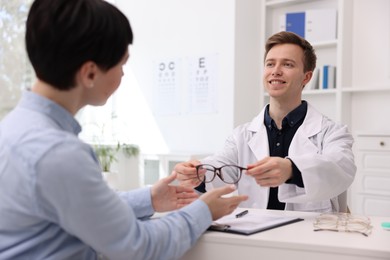 Photo of Ophthalmologist giving glasses to patient at white table in clinic