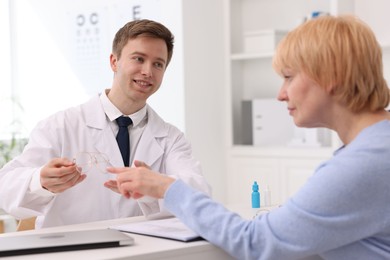 Photo of Ophthalmologist consulting senior woman at white table in clinic