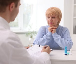 Photo of Ophthalmologist consulting senior woman at white table in clinic