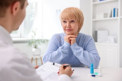 Photo of Ophthalmologist consulting senior woman at white table in clinic