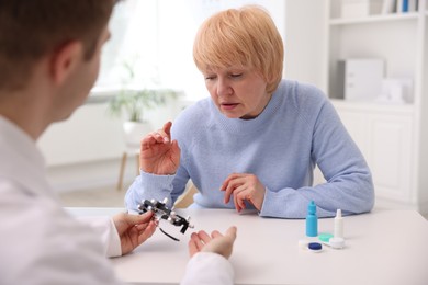 Photo of Ophthalmologist consulting senior woman at table in clinic