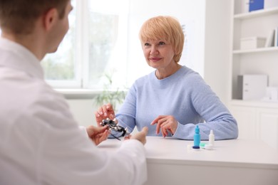 Photo of Ophthalmologist consulting senior woman at table in clinic