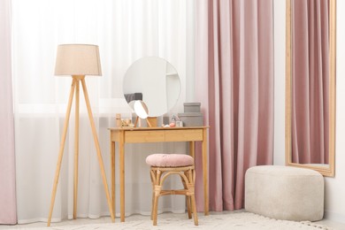 Image of Mirrors, dressing table, lamp and stool near window with pink beige curtains in room. Interior design