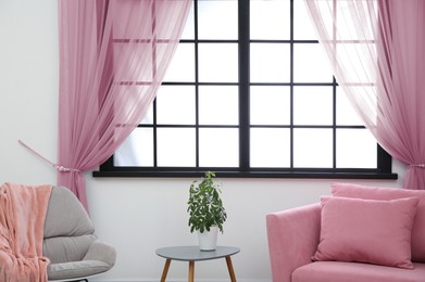 Image of Armchair and sofa near window with pink curtains in room. Interior design