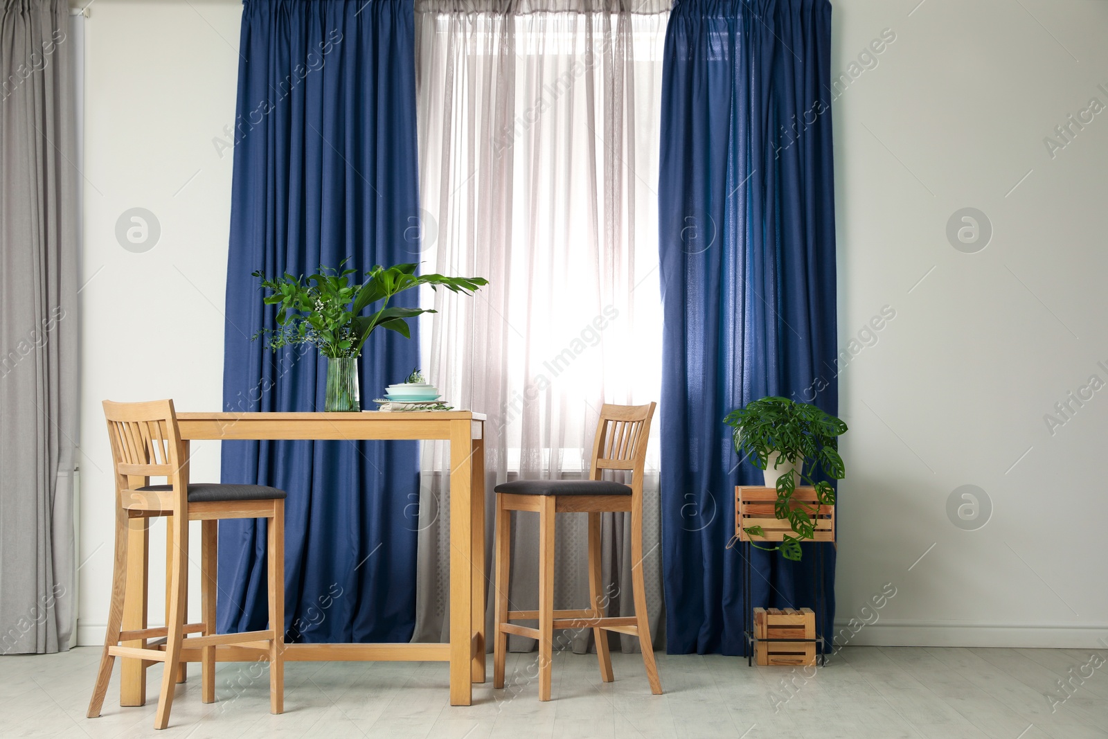 Dining table and chairs near window with blue curtains in room. Interior design Image of Dining table and chairs near window with blue curtains in room. Interior design