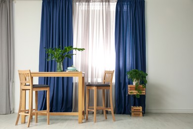 Image of Dining table and chairs near window with blue curtains in room. Interior design