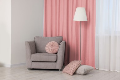 Image of Comfortable armchair and floor lamp near window with pink curtains in room. Interior design