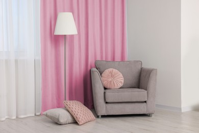 Image of Comfortable armchair and floor lamp near window with pink curtains in room. Interior design