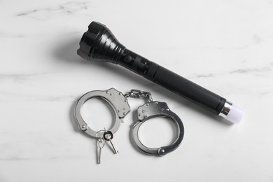 Photo of Flashlight, handcuffs and keys on white marble table, flat lay. Police equipment