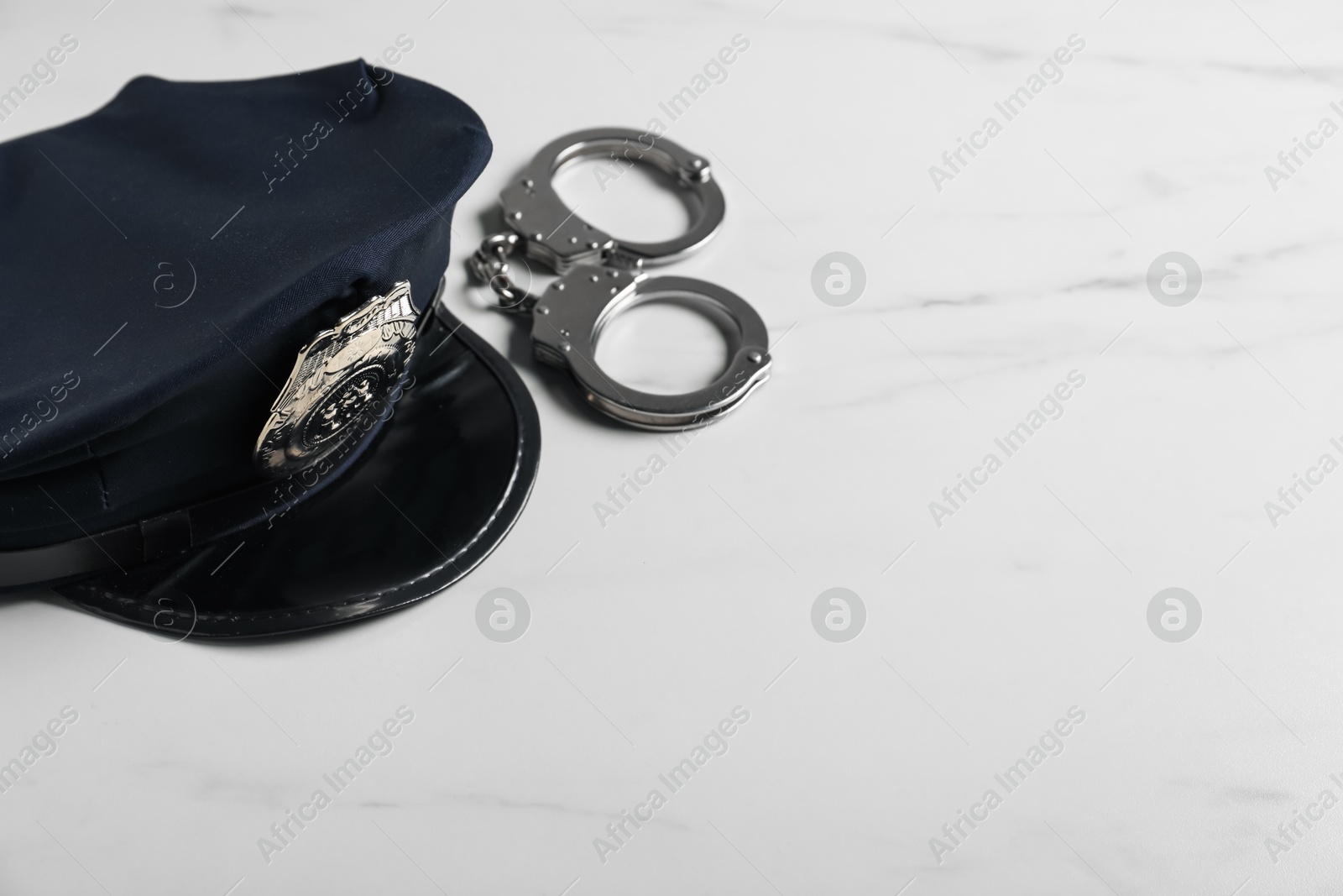 Police cap and handcuffs on white marble table, closeup. Space for text Photo of Police cap and handcuffs on white marble table, closeup. Space for text