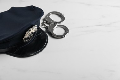 Photo of Police cap and handcuffs on white marble table, closeup. Space for text