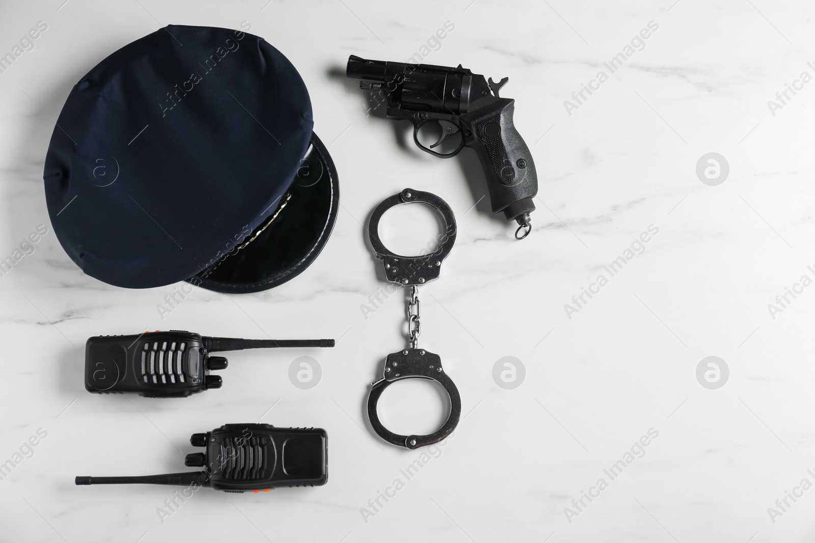 Police cap, gun, handcuffs and walkie talkie on white marble table, flat lay. Space for text Photo of Police cap, gun, handcuffs and walkie talkie on white marble table, flat lay. Space for text