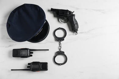 Photo of Police cap, gun, handcuffs and walkie talkie on white marble table, flat lay. Space for text