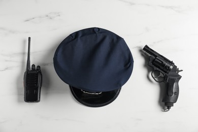 Photo of Police cap, gun and walkie talkie on white marble table, flat lay