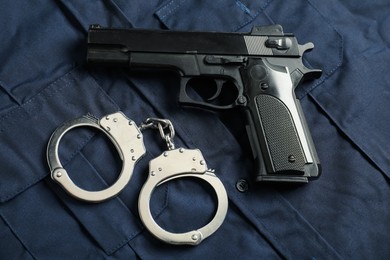 Photo of Black gun and handcuffs on dark blue uniform, above view. Police equipment