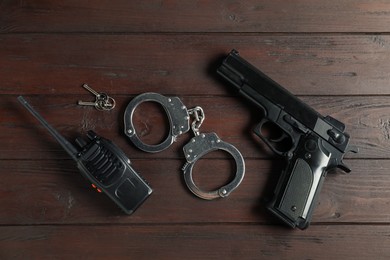 Photo of Walkie talkie, handcuffs, gun and keys on wooden table, flat lay. Police equipment