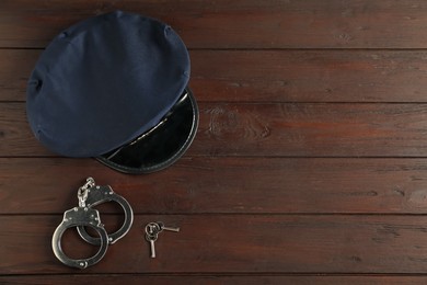 Photo of Police cap, handcuffs and keys on wooden table, flat lay