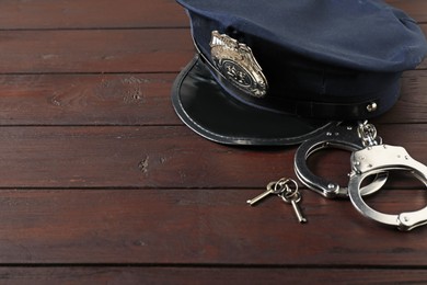 Photo of Police cap, handcuffs and keys on wooden table, closeup. Space for text