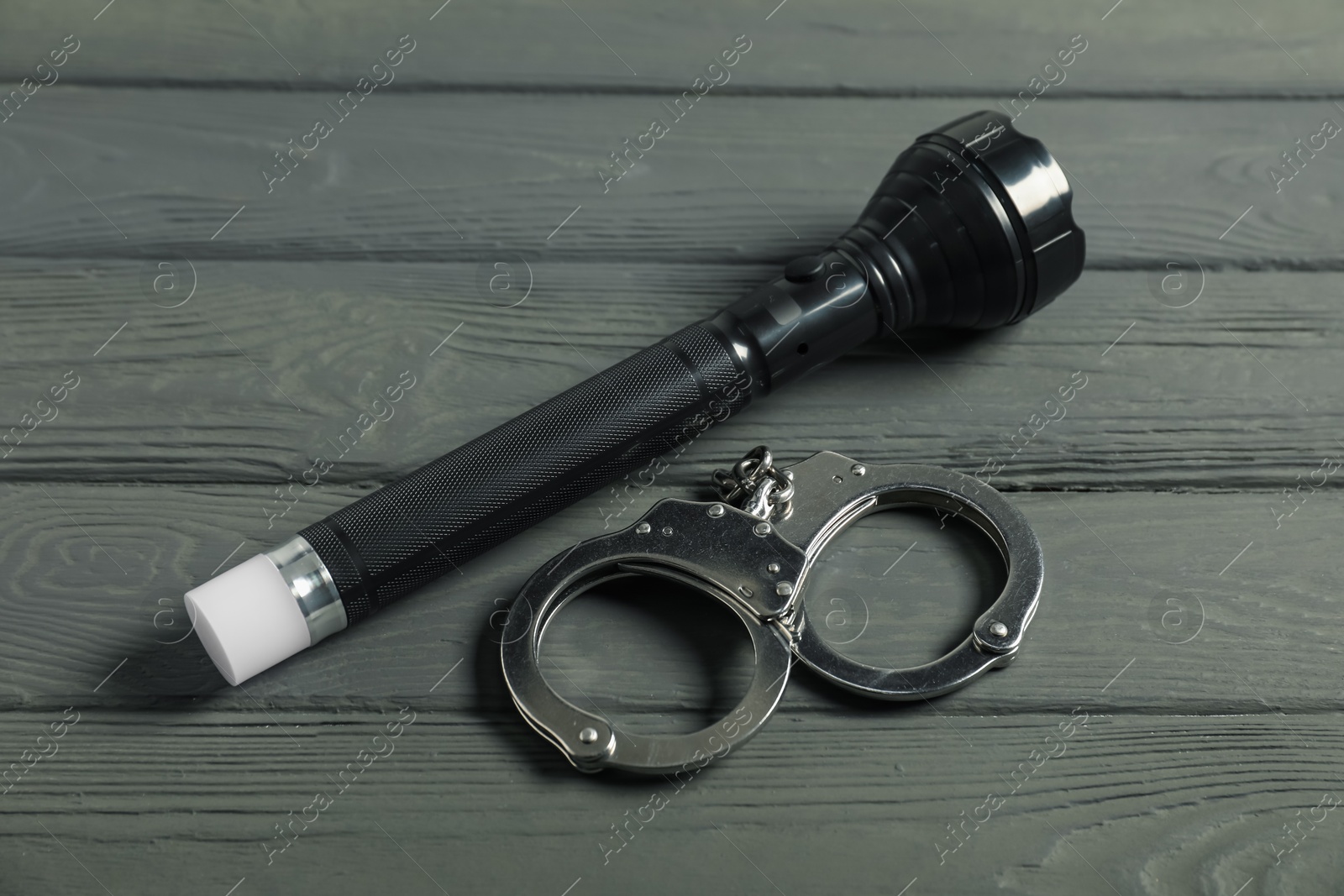 Flashlight and handcuffs on grey wooden table, closeup. Police equipment Photo of Flashlight and handcuffs on grey wooden table, closeup. Police equipment
