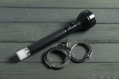 Photo of Flashlight and handcuffs on grey wooden table, closeup. Police equipment