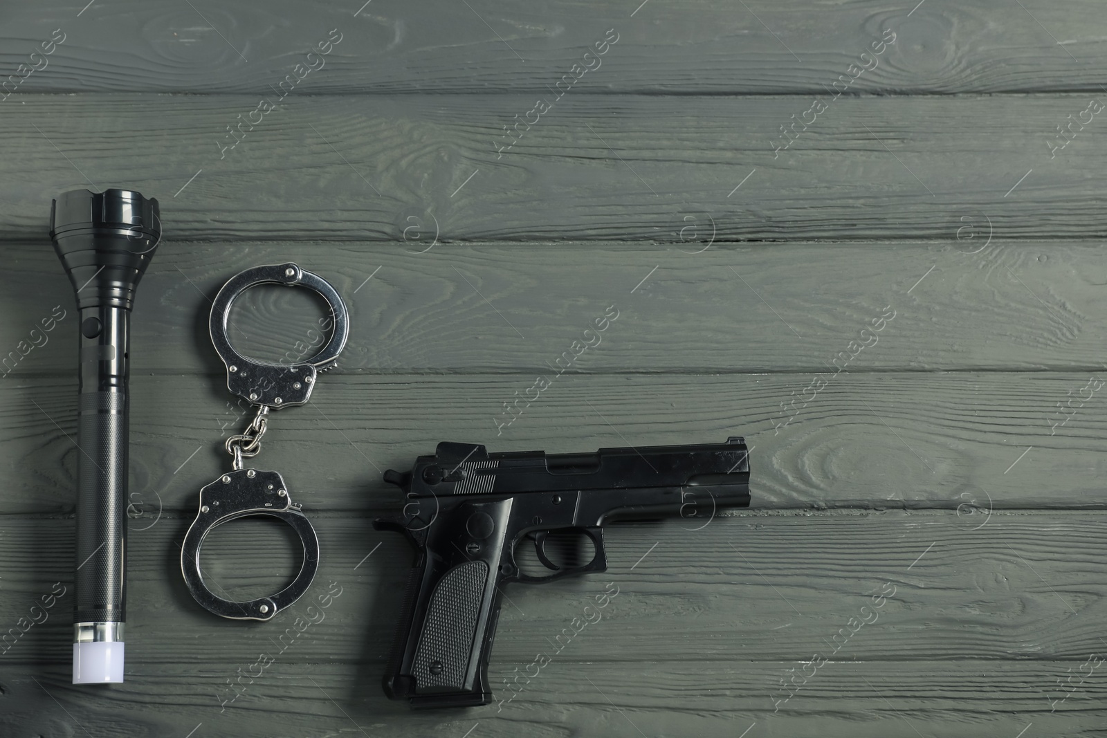 Police equipment. Gun, handcuffs and flashlight on grey wooden table, flat lay. Space for text Photo of Police equipment. Gun, handcuffs and flashlight on grey wooden table, flat lay. Space for text
