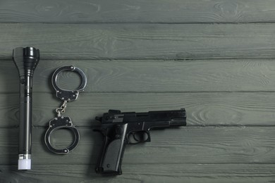 Photo of Police equipment. Gun, handcuffs and flashlight on grey wooden table, flat lay. Space for text