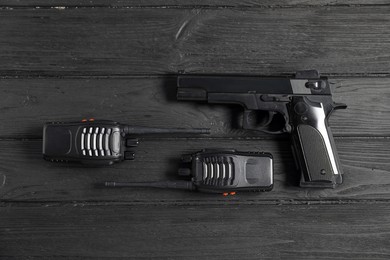 Photo of Gun and walkie talkies on black wooden table, flat lay. Police equipment