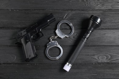 Photo of Gun, handcuffs and flashlight on black wooden table, flat lay. Police equipment