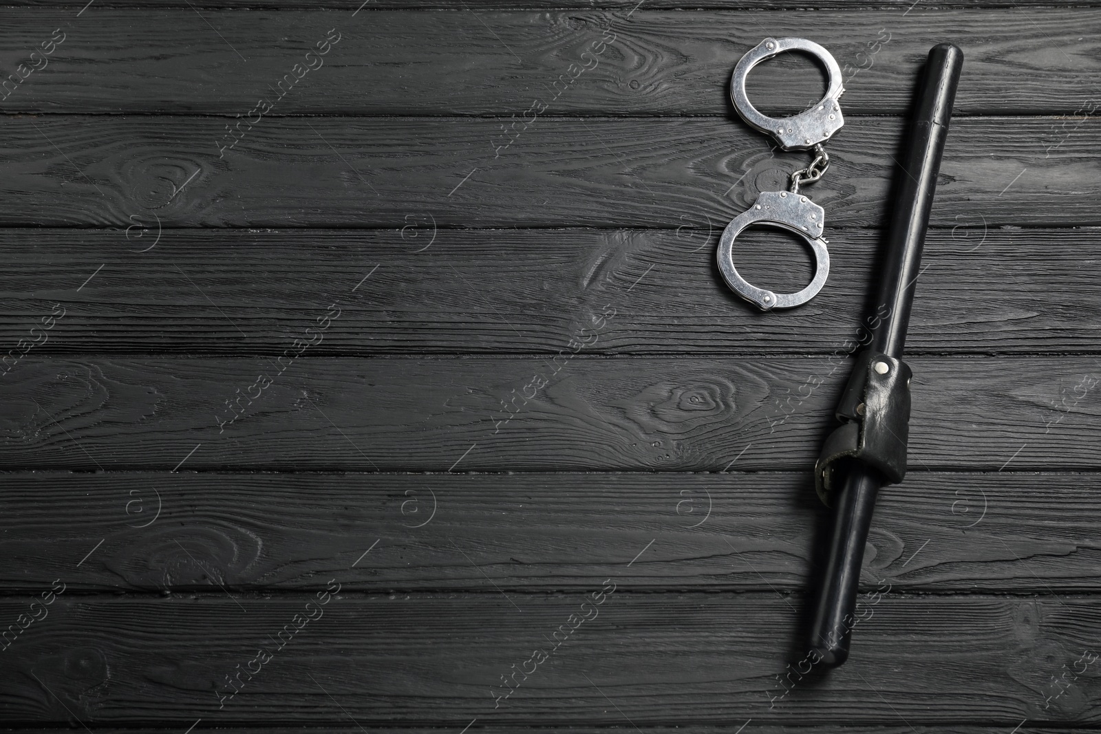 Photo of Police baton and handcuffs on black wooden table, flat lay. Space for text