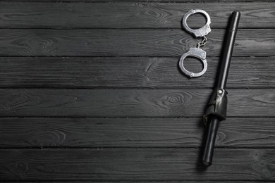 Photo of Police baton and handcuffs on black wooden table, flat lay. Space for text