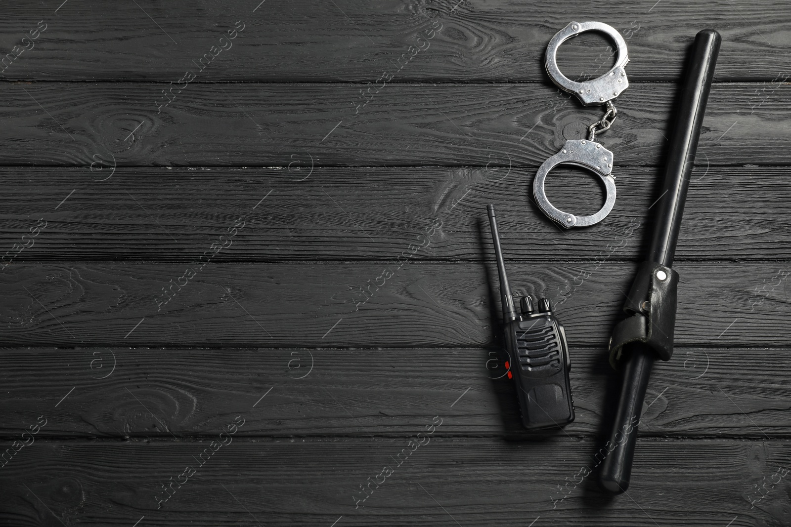 Photo of Police baton, walkie talkie and handcuffs on black wooden table, flat lay. Space for text