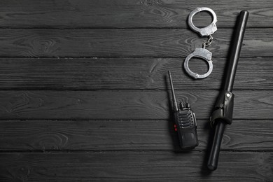 Photo of Police baton, walkie talkie and handcuffs on black wooden table, flat lay. Space for text