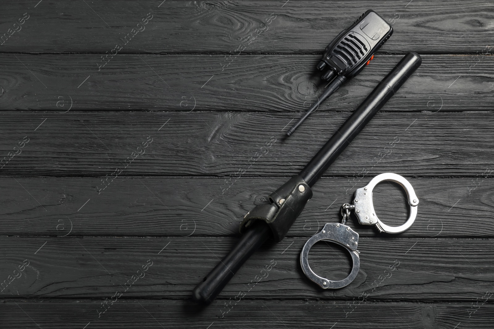Photo of Police baton, walkie talkie and handcuffs on black wooden table, flat lay. Space for text
