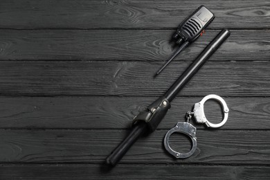 Photo of Police baton, walkie talkie and handcuffs on black wooden table, flat lay. Space for text