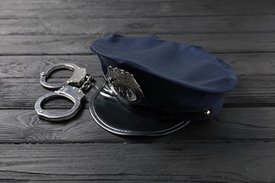 Photo of Police cap and handcuffs on black wooden table, closeup