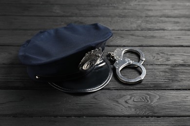 Photo of Police cap and handcuffs on black wooden table, closeup
