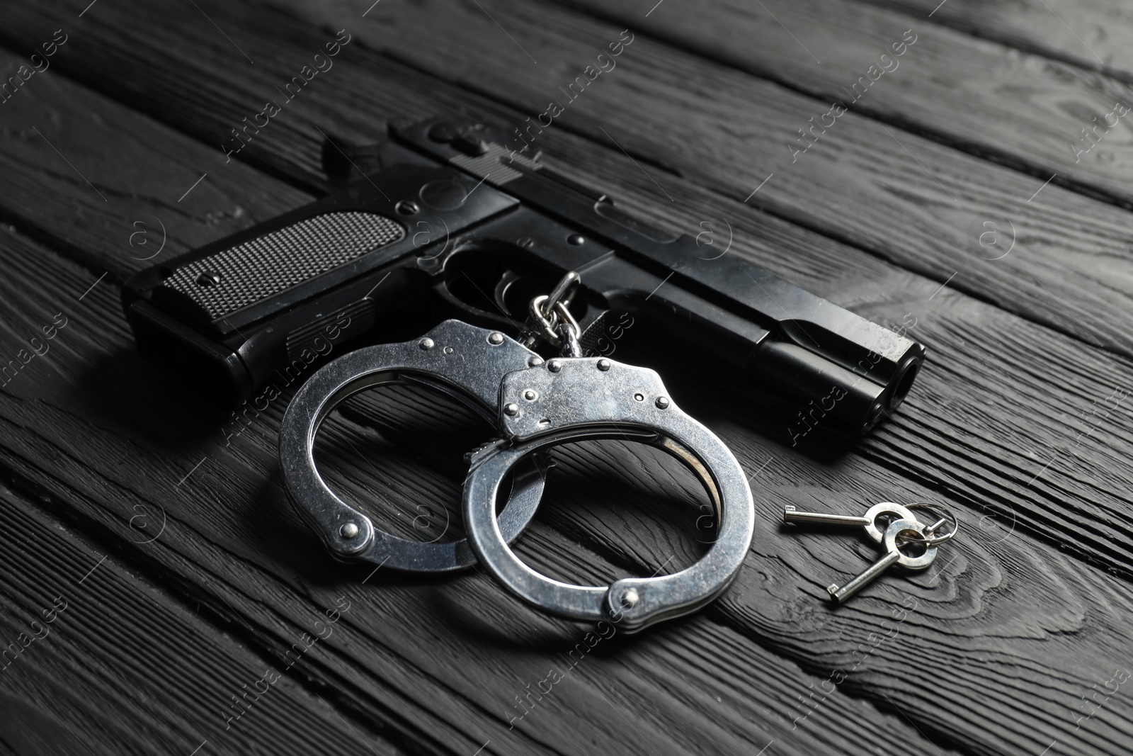 Gun, handcuffs and keys on black wooden table, closeup. Police equipment Photo of Gun, handcuffs and keys on black wooden table, closeup. Police equipment