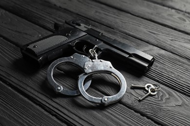Photo of Gun, handcuffs and keys on black wooden table, closeup. Police equipment