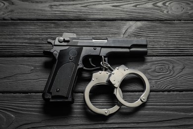 Photo of Gun and handcuffs on black wooden table, flat lay. Police equipment