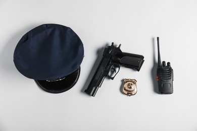 Photo of Police cap, gun, badge and walkie talkie on white background, flat lay