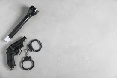 Photo of Gun, handcuffs and flashlight on light grey table, flat lay. Space for text