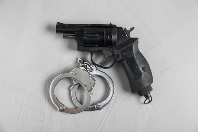 Photo of Gun and handcuffs on light grey table, flat lay