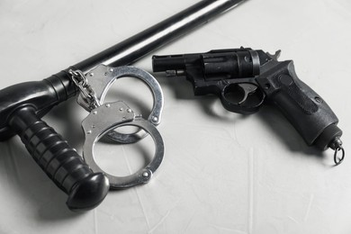 Photo of Police baton, handcuffs and gun on light grey table, closeup