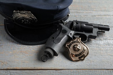 Photo of Police cap, gun and badge on grey wooden table, closeup