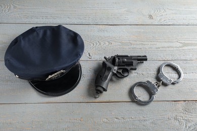 Photo of Police cap, gun and handcuffs on grey wooden table, flat lay