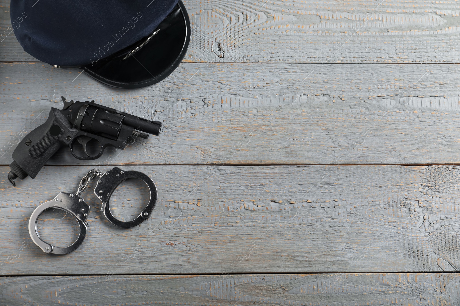 Police cap, gun and handcuffs on grey wooden table, flat lay. Space for text Photo of Police cap, gun and handcuffs on grey wooden table, flat lay. Space for text