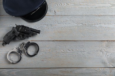 Photo of Police cap, gun and handcuffs on grey wooden table, flat lay. Space for text