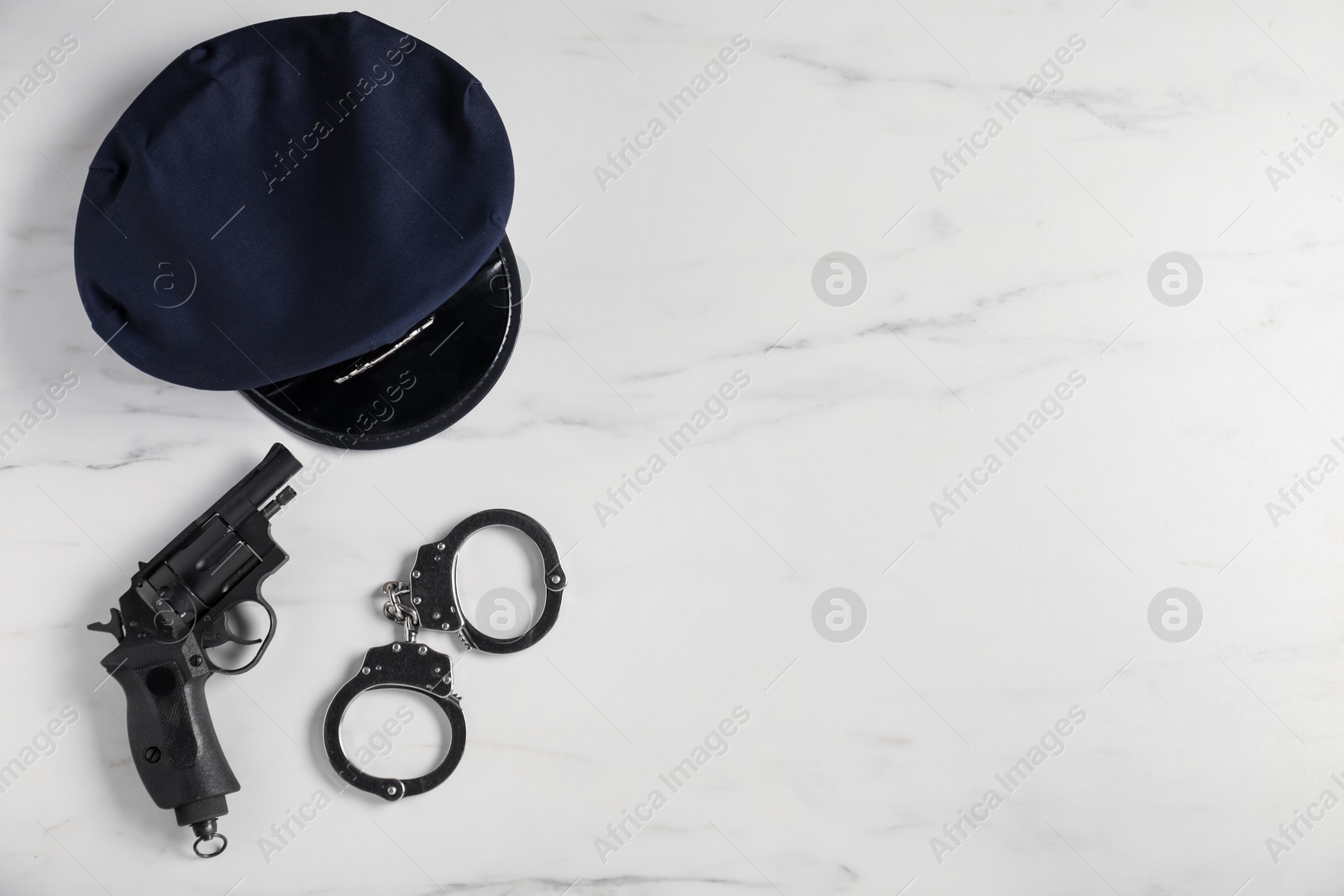 Police cap, gun and handcuffs on white marble table, flat lay. Space for text Photo of Police cap, gun and handcuffs on white marble table, flat lay. Space for text