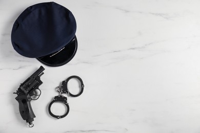Photo of Police cap, gun and handcuffs on white marble table, flat lay. Space for text